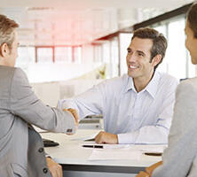 ein Frau und zwei Männer an einem Bürotisch im Beratungsgespräch, die beiden Männer reichen sich soeben die Hände